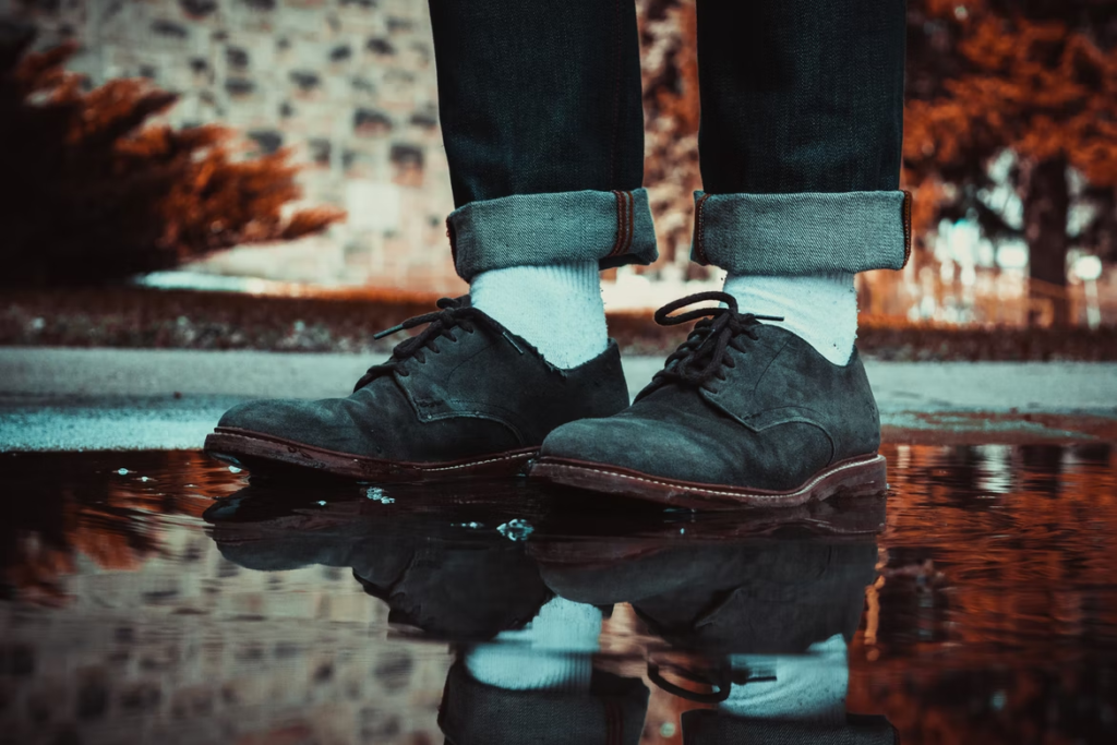 Prikaz muških cipela od brušene kože kako stoje u lokvi vode na cesti.