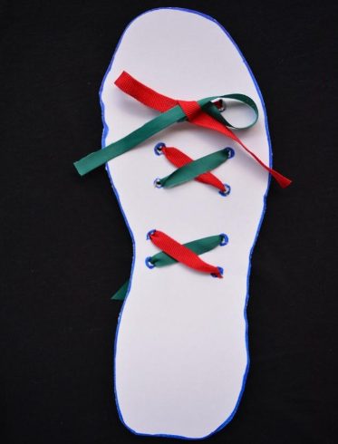 Karton oblikovan poput uloška za cipele s crvenom i zelenom vrpcom na kojem dijete može vježbati vezanje cipela.