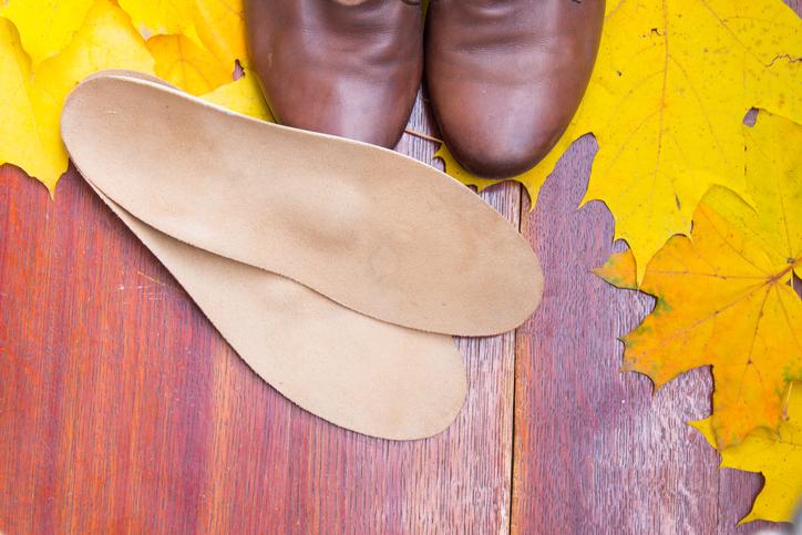 Prikaz smeđih kožnih cipela i kožnih uložaka na smeđoj podlozi ukrašenoj žutim lišćem.