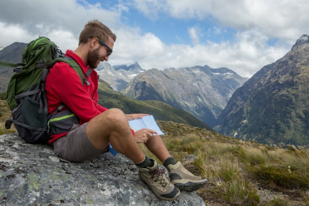 Prikaz muškarca odjevenog u planinarsku odjeću kako odmara na vrhu planine.