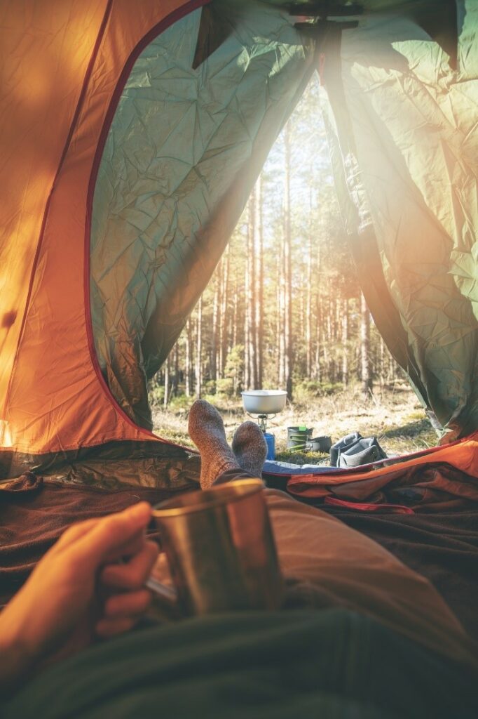 Prikaz osobe u vunenim čarapama za planinarenje kako odmara u šatoru negdje u prirodi.