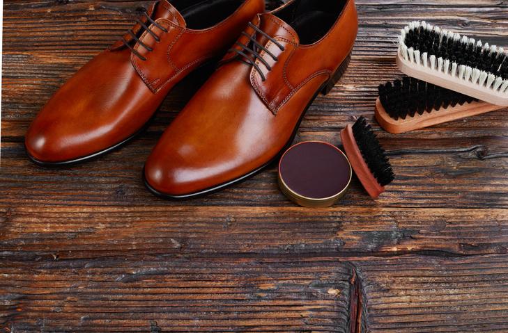 Prikaz smeđih kožnih cipela za muškarce pored kojih stoje četke za cipele i sredstva za njegu obuće.