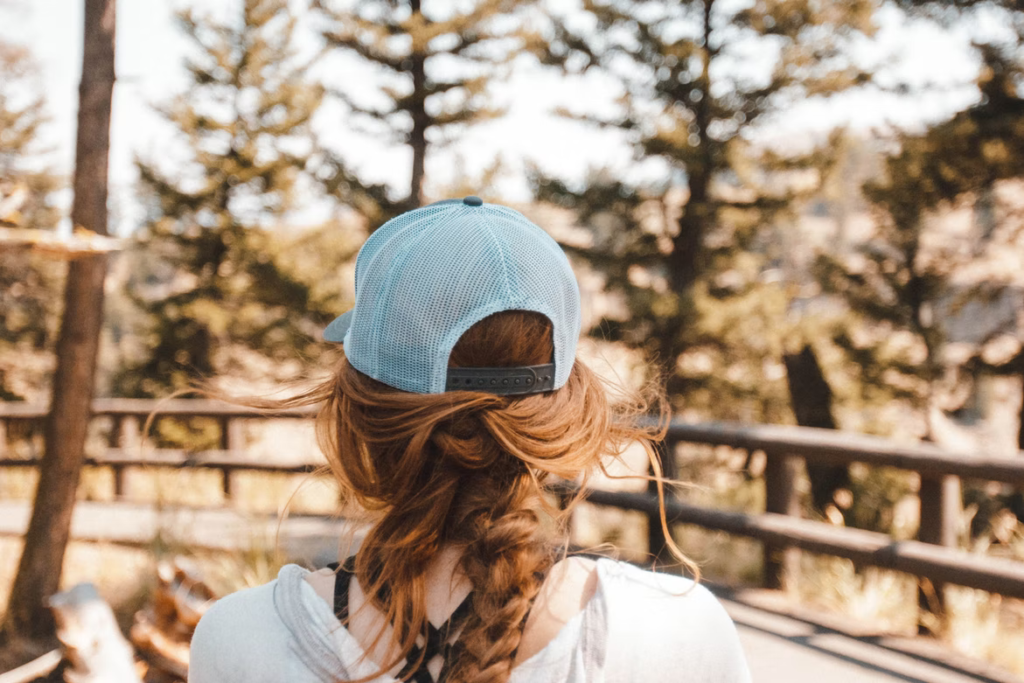 Žena u šumi, okrenuta leđima, s plavom šiltericom na glavi.