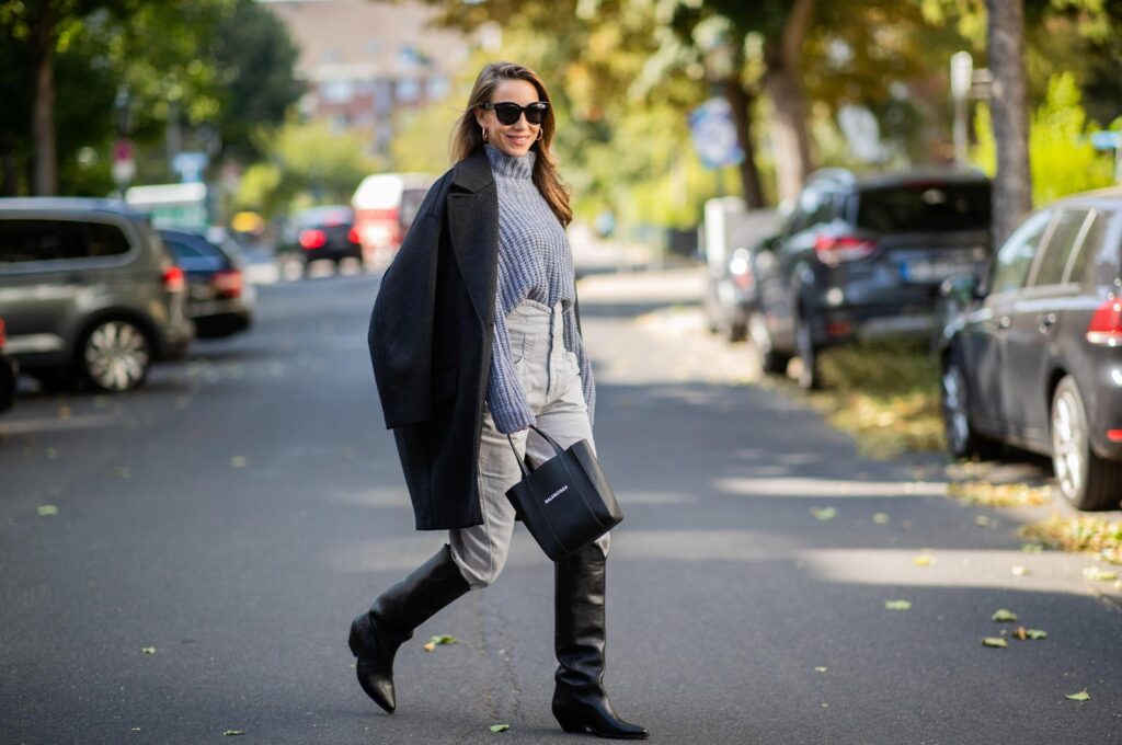 Prikaz outfita složenog od pulovera i traperica koji upotpunjuju crne visoke kaubojske čizme te crni kaput i torbica.