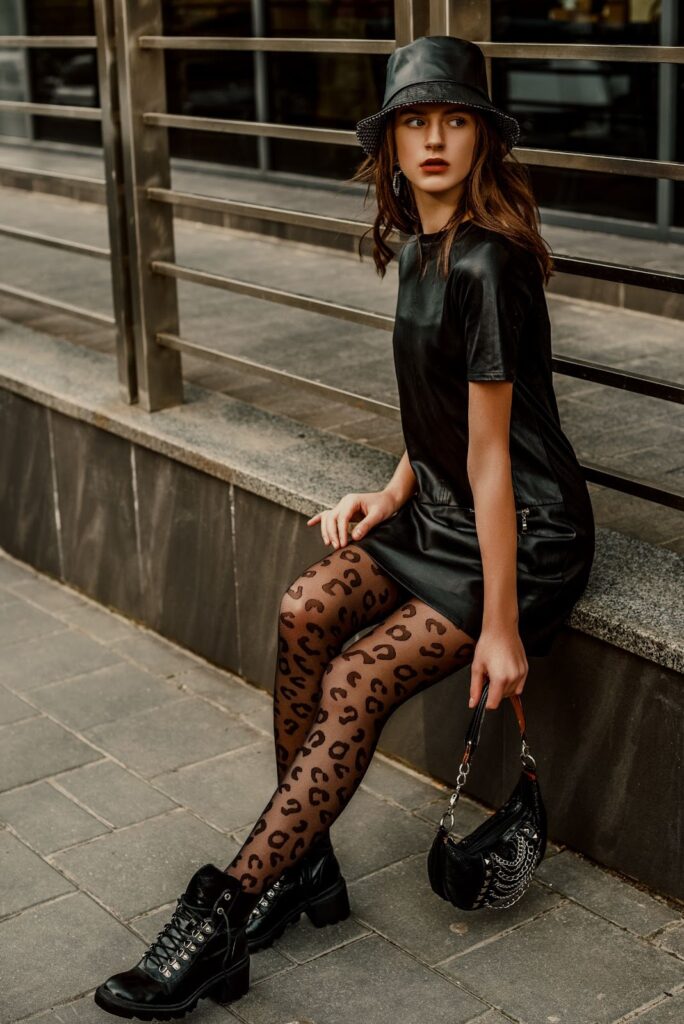 Djevojka u crnom total look outfitu nosi crne čarape s uzorkom na leopardove točkice i crne gležnjače s debelim potplatom.