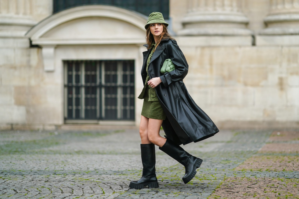 Model je odjeven u kombinaciju suknje i sakoa maslinasto zelene boje koja se savršeno slaže s crnim dugim kaputom i crnim masivnim čizmama. Cijela kombinacija upotpunjena je šeširom i torbicom u maslinastoj boji.