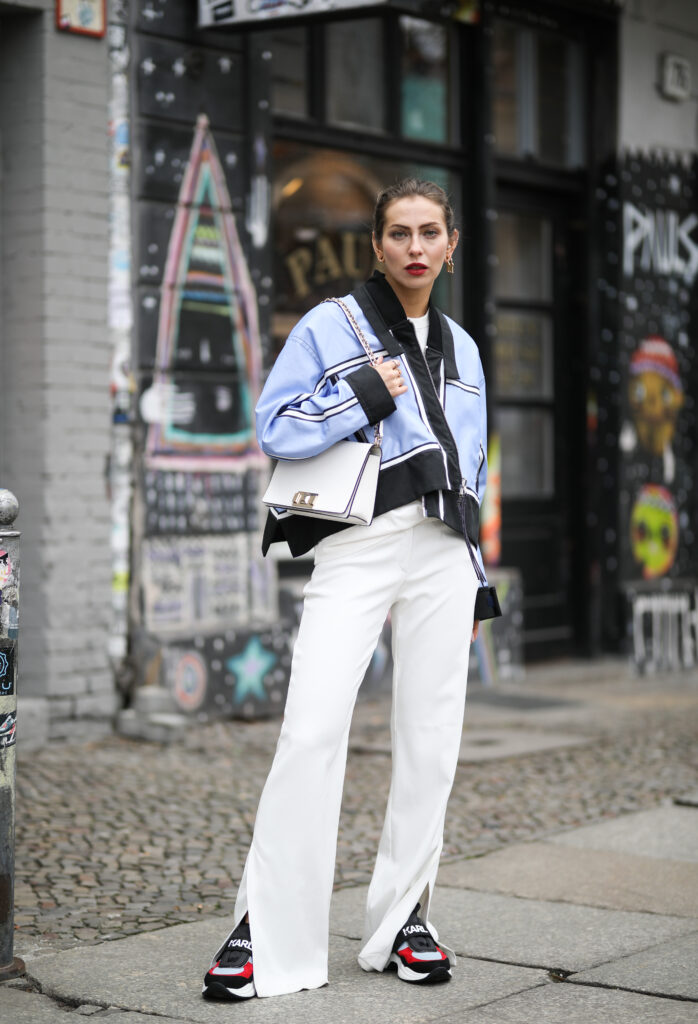 Djevojka na sebi nosi Karl Lagerfeld sneakersice uz kombinaciju plave jakne i bijelih elegantnih hlača. Odabrala je model tenisica s trakom na kojoj je logo brenda.