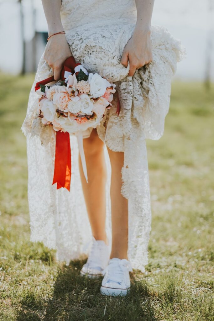 Žena u boho vjenčanici s buketom cvijeća u ruci u niskim bijelim tenisicama